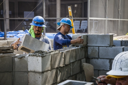 two people wearing hardhats stacking concrete blocks on a construction site